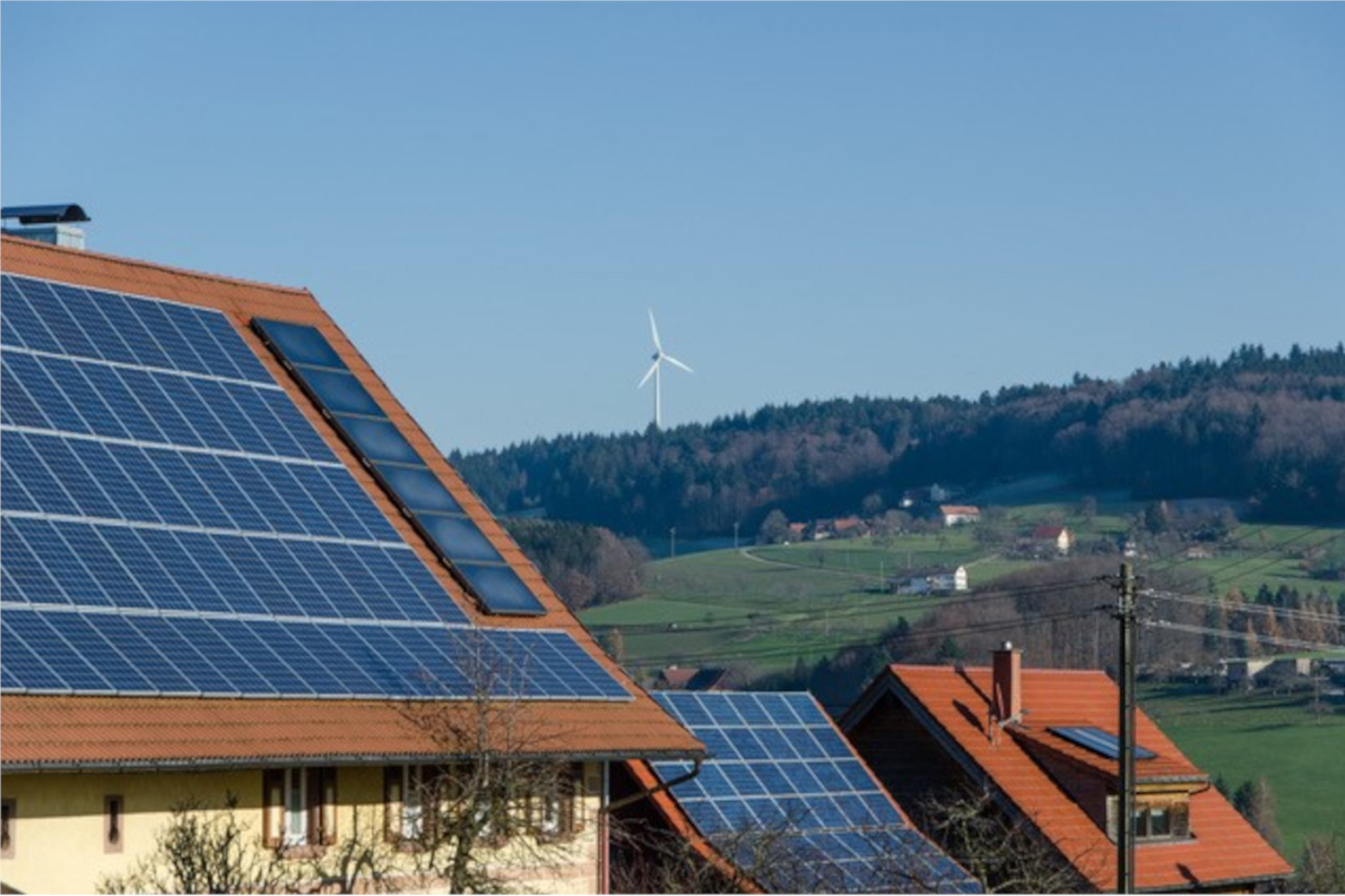 Solarzellen auf Hausdächern, dahinter ein Windrad