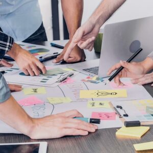 Gruppenarbeitssituation: Arbeitstisch mit Plakat und Post-Its und Händen von 5 Personen mit Laptop und Tablet