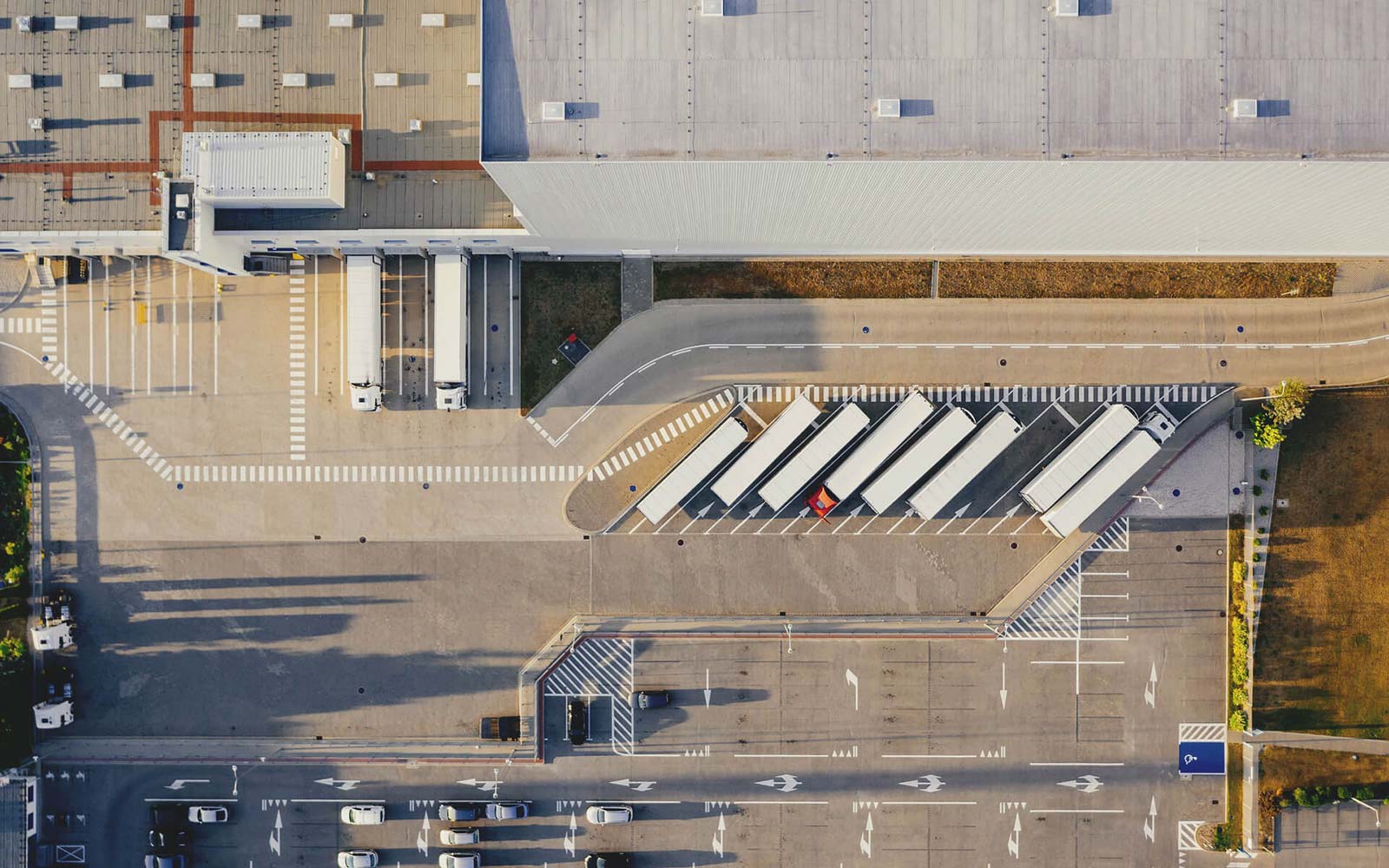 Unternehmensgelände mit LKWs, die an Rampe aus der Produktion beladen werden und PKWs auf Parkplatz in Vogelperspektive