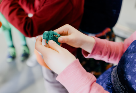 Kinderhände halten eine 3D-gedruckte Figur des FZI-Roboters HoLLiE